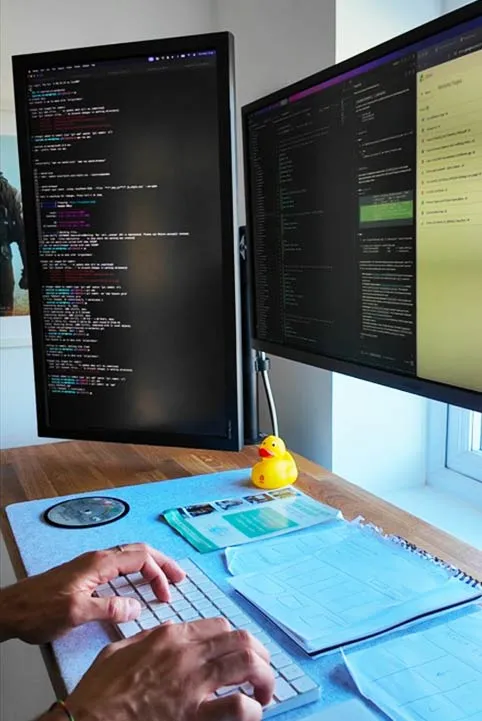 A developer's desk with code open on two monitors